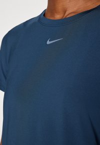 Camiseta de cuello redondo de color azul marino, fabricada en un tejido suave y transpirable que presenta un discreto logo de Nike en gris en el pecho. Mangas cortas.