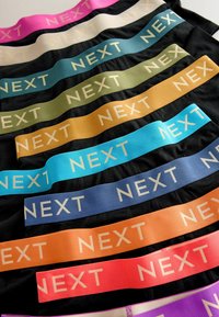 Teanc de lenjerie neagră cu talie elastică în culori variate, fiecare având eticheta „NEXT” cu litere mari și contrastante.