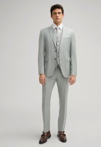 Helles graues dreiteiliges Anzugset mit maßgeschneiderter Jacke, Weste und Hose. Verfügt über eine subtile Textur, Reverskragen und braune Lederschuhe.