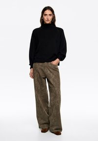 Czarny dziany golf z prążkowanymi mankietami w połączeniu z szerokimi oliwkowozielonymi spodniami o delikatnym teksturowanym wzorze. Brązowe zamszowe buty.