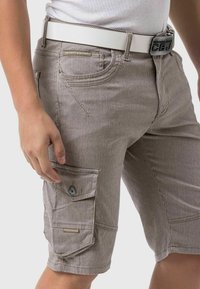 Beige striped cargo shorts with a side pocket, textured fabric, and a white belt. Features a brand label on the front pocket.