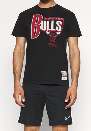 Musta puuvillainen T-paita, jossa on punaisella ja valkoisella teksti "CHICAGO BULLS", härkägrafiikka ja "Windy City" -yksityiskohta. Lyhythihaiset ja pyöreä kaula-aukko.