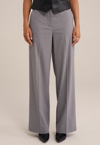 Pantalones grises de pierna ancha con un ajuste entallado, que presentan una textura suave y pliegues frontales, combinados con tacones negros puntiagudos.