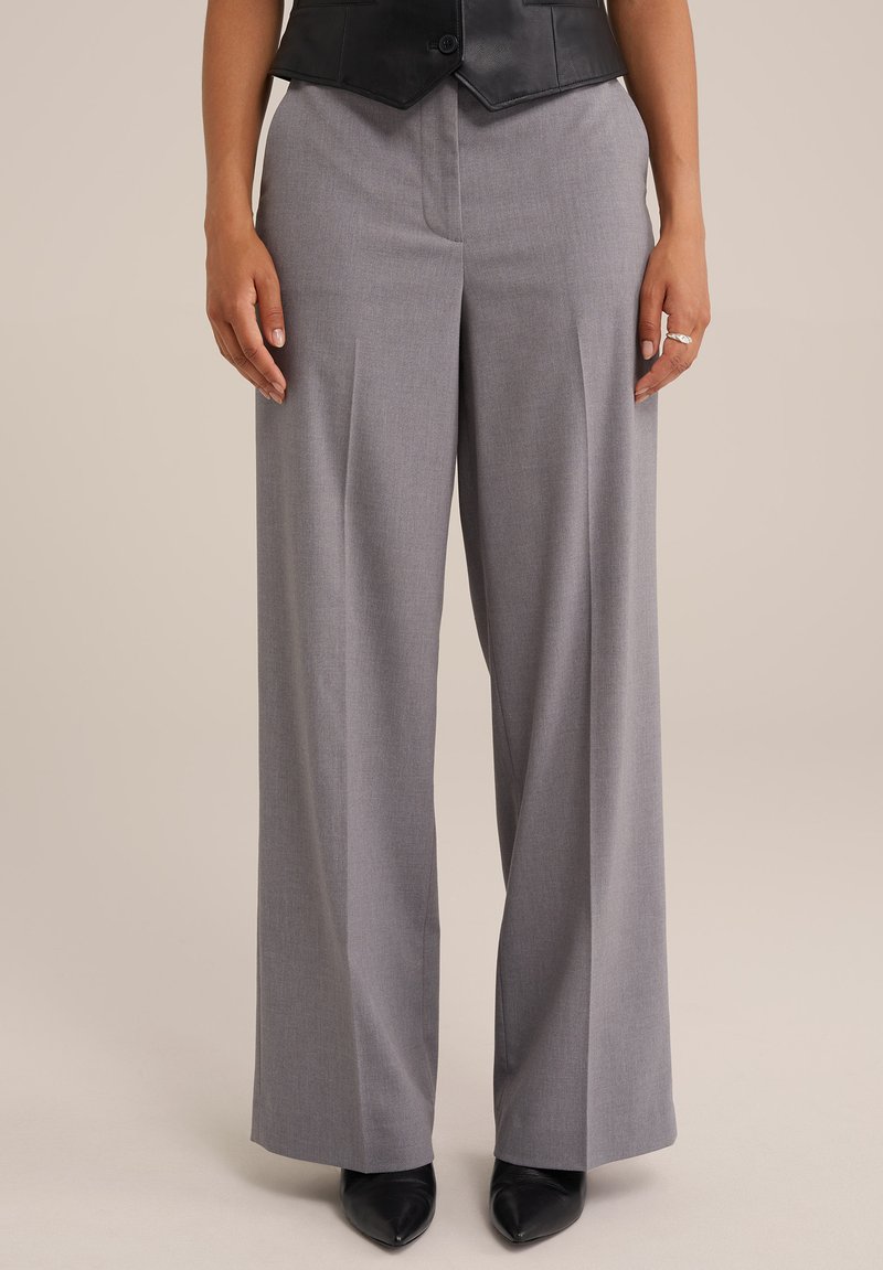 Pantalones grises de pierna ancha con un ajuste entallado, que presentan una textura suave y pliegues frontales, combinados con tacones negros puntiagudos.