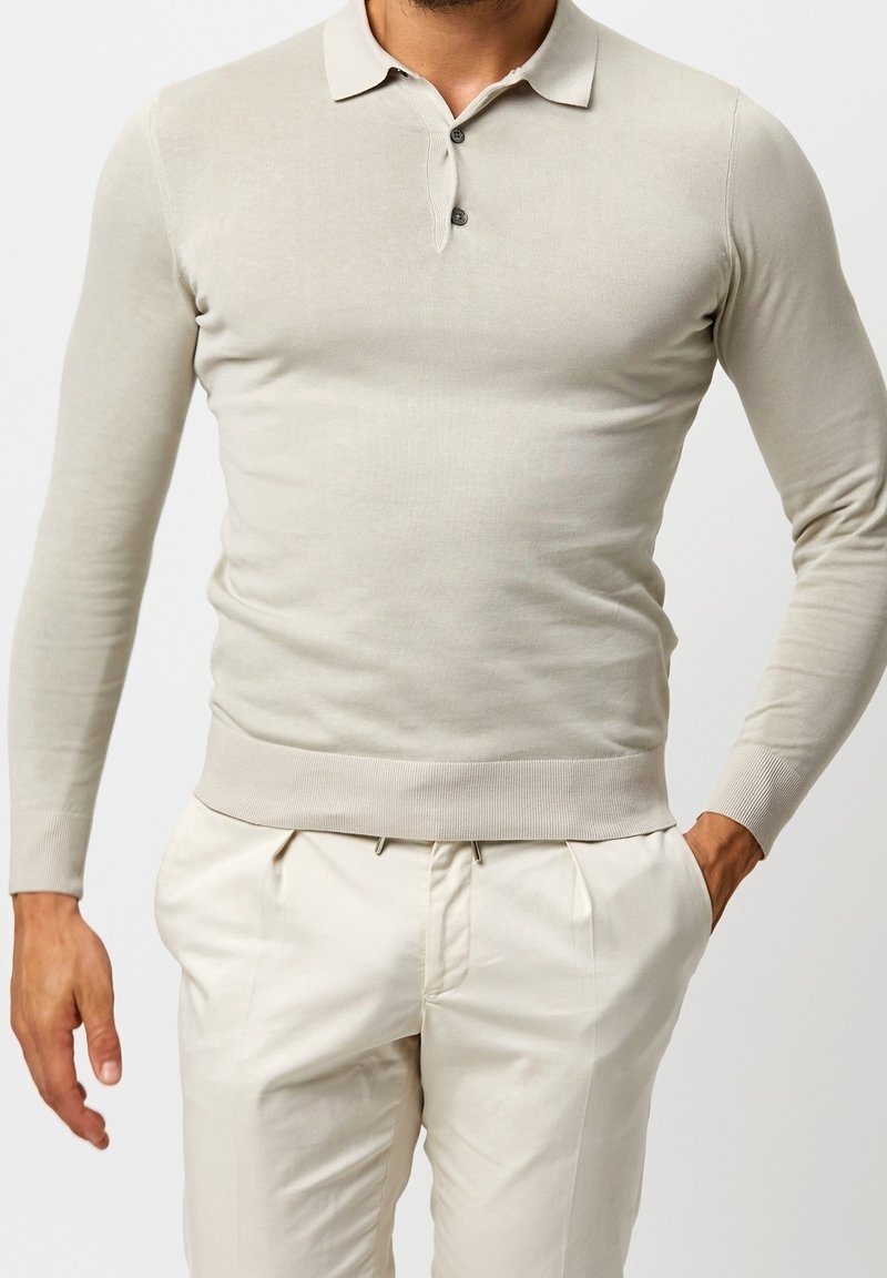 Beige polo s dlouhým rukávem, límečkem, dvoubUTTONOVOU légou a žebrovanými manžetami. Hladký materiál, upnutý střih, kombinovaný s kalhotami světlejší barvy.