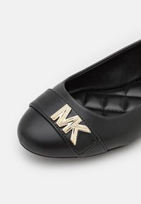 Chaussure plate en cuir noir avec une semelle matelassée et un logo MK doré sur la bride avant.