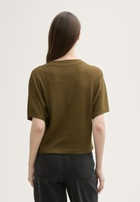 Top scurt de culoare verde măslinie, cu un design texturat și nervurat, având un guler rotund și o croială lejeră, asortat cu blugi din denim închis.
