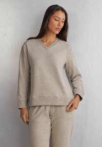 Beige sweatshirt met lange mouwen en een V-hals, met een textuur en een chevronpatroon aan de onderkant. Zacht materiaal met een relaxte fit.