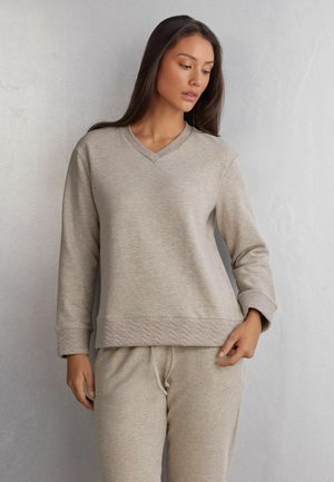 Beige långärmad sweatshirt med V-ringning, med en texturerad, chevron-mönstrad nederkant. Mjuk tyg med avslappnad passform.