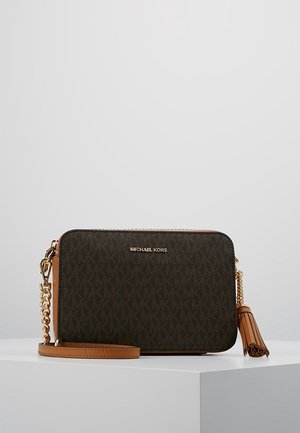 Ciemnobrązana torba na ramię Michael Kors z złotym łańcuszkiem, jasnobrązowymi skórzanymi akcentami, nadrukiem logo i frędzelkami na białej powierzchni.