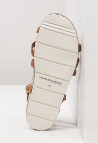 Tan leather straps with a braided texture, featuring a white rubber sole. Stamped branding and size marked on the bottom.