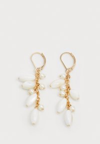 Des boucles d'oreilles pendantes en ton or présentent plusieurs perles ovales blanches et petites perles, disposées dans un design en cascade sur une chaîne articulée.