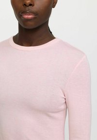 Light pink long-sleeve t-shirt made of soft fabric with a round neckline and ribbed texture, showcasing a simple, smooth design.