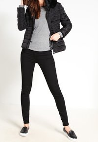 Černá péřová bunda s umělým kožíškem, šedé dlouhé tričko, černé slim džíny a černé slip-on boty. Hladká textura a přizpůsobený střih.