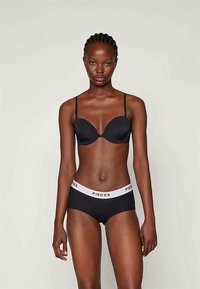 Schwarzer gepolsterter BH mit schmalen Trägern, kombiniert mit schwarzen Hipster-Höschen mit einem weißen Bund, auf dem der Text "PIECES" steht. Glatte Textur.