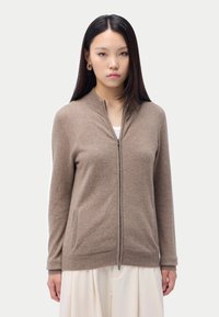 Brun zip-up cardigan tillverkad av mjukt material med rund halsringning, sidofickor och ribbade ärmslut med en jämn yta.