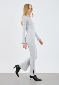 Hellgrau gestreiftes Strick-Zweiteiler-Set mit einem figurbetonten Langarmtop und weit geschnittenen Hosen mit seitlichen Schlitzen, kombiniert mit schwarzen High-Heel-Stiefeln.