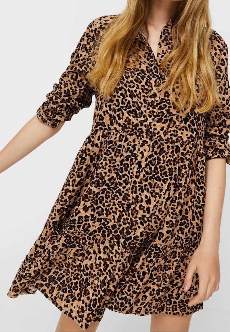 Sukienka koszulowa w panterkę w kolorze tan i czarnym, z guzikiem z przodu, długimi rękawami i falbanistym, zwiewnym dołem. Miękka struktura materiału.