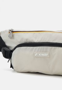 Pilkai K-Way maišelis su tekstūriniu paviršiumi, turintis juodą užtrauktuko kišenę, oranžinį akcentą ir logotipo pleistrą. Kompaktiškas ir funkcionalus dizainas.
