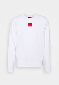 Valkoinen collegepaita, joka on valmistettu puuvillasta, pitkillä hihoilla ja pyöreällä kaula-aukolla. Rinnassa on punainen suorakulmainen logopatch.