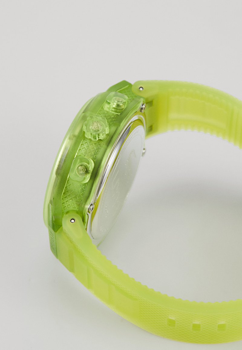 Reloj de plástico verde translúcido con caja redonda, banda texturizada y tres botones de presión; cuenta con una esfera de color plateado en el lado posterior.