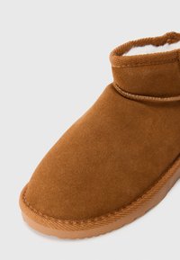 Brune semsket ankelstøvle med blødt hvidt fleecefor og tekstureret gummisål, designet til varme og komfort.
