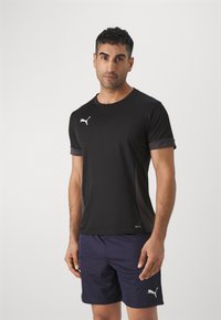 T-shirt atlético preto com punhos roxos contrastantes, apresentando um logotipo branco no peito; usado com calções escuros.