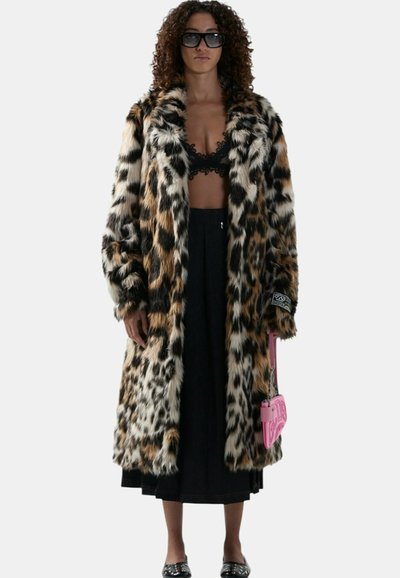 Vrouw draagt een oversized bontjas met luipaardprint, een zwarte kanten bralette, een zwarte midi-rok, een zonnebril en houdt een roze handtas vast.