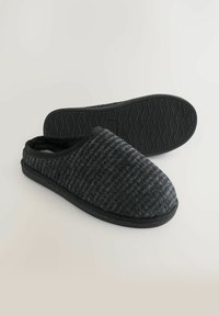 Zwarte gebreide slippers met een gestructureerde bovenkant, ronde neus en rubberen zool met een golfpatroon voor grip. Zachte voering aan de binnenkant.