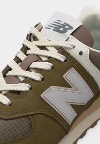 Gros plan d'une basket New Balance marron et beige avec des lacets blancs et un logo sur le côté et sur la languette.