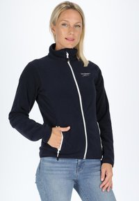 Marinblå fleecejacka med hög krage, hel frontdragkedja och sidofickor. Har vita dragkedjestråkar och en logotyp på bröstet.