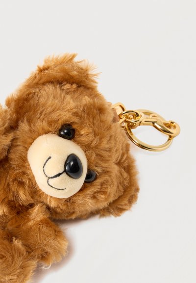 Καφέ μαλακό μπρελόκ αρκουδάκι με χρυσό μεταλλικό κούμπωμα σε απλό λευκό φόντο.