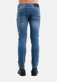 Jeans di jeans blu con vestibilità slim, con due tasche posteriori, lievi striature e taglio dritto alle caviglie. Indossati con stivali neri.