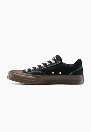 Schwarze low-top Sneaker mit weißen Schnürsenkeln, weißen Nähten und einer braunen Gummisohle sowie einer Gummikappe auf einem weißen Hintergrund.