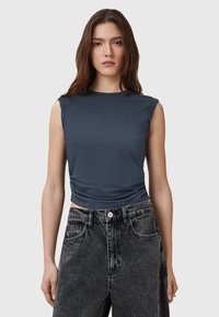 Dark blue sleeveless top with a high neckline, featuring side ruching and soft, lightweight fabric. Paired with high-waisted black denim shorts.