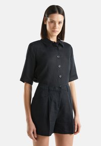 Camicia nera in lino con colletto, maniche corte e bottoni frontali, abbinata a pantaloni corti coordinati con una vestibilità sartoriale e tasche laterali.