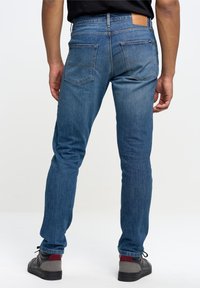 Blå denimjeans med rak passform, som har en läderlapp på baksidan av midjan och två bakfickor. Bärs med grå och röda sneakers.