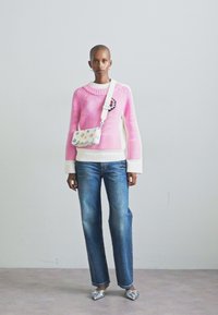 Pink knitted sweater with white accents, blue straight-leg jeans, and silver shoes. Small floral crossbody bag is worn across the body.