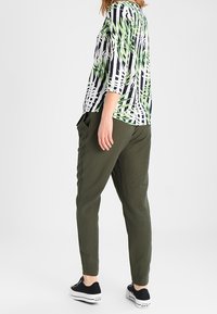 Top verde e nero con motivo, maniche a tre quarti, abbinato a pantaloni a sigaretta verde oliva e sneakers nere.