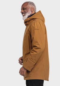 Braune wasserfeste Jacke mit Kapuze, ausgestattet mit einem Frontreißverschluss, Seitentaschen und einer glatten Textur. Markenname "Schöffel" auf dem Ärmel.