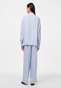 Camisa de lino azul claro y pantalones de pierna ancha, con un corte relajado, tejido ligeramente texturizado y detalle de yugo en la parte posterior.
