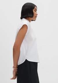Camicia bianca a maniche corte con orlo curvo, realizzata in tessuto liscio. Il design presenta un colletto classico e una vestibilità rilassata.