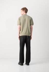 Khaki polo tričko s krátkym rukávom a priliehavým strihom, s ribovaným golierom a elastickým lemom. V kombinácii s voľnými čiernymi džínsami a pevnými topánkami.