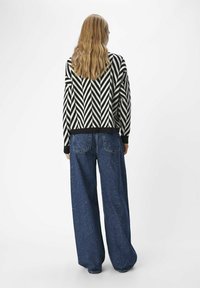 Svart och vit chevronmönstrad tröja med ribbad mudd, kombinerad med löst sittande blå denimjeans med bakfickor.
