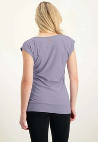 Lavender Kurzarmoberteil mit rundem Ausschnitt, figurbetontem Design und einem Logo-Detail im Rückenbereich. Weicher Stoff und glatte Textur.