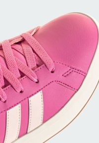 Pinker Sneaker mit strukturierten Schnürsenkeln, weißen Seitenstreifen und weißer Sohle mit hellbraunem Rand, Nahaufnahme auf hellem Hintergrund.