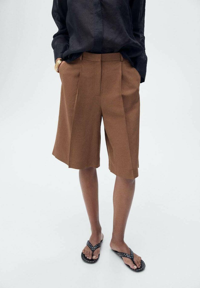 Bruna veckade shorts gjorda av ett strukturerat tyg, midj längd, har sidofickor, i kombination med svarta flip-flops.