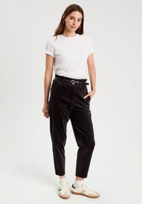 Pantalons en velours côtelé noir taille haute avec poches latérales, taille cintrée avec une ceinture noire, associés à un t-shirt blanc et des baskets blanches.