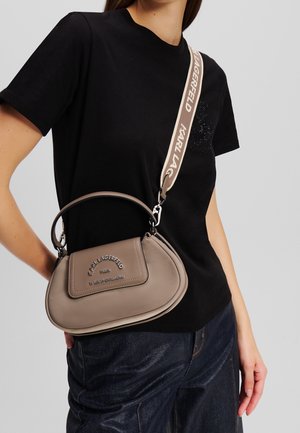 Kvinde iført sort T-shirt og mørke jeans, bærende en taupe Karl Lagerfeld håndtaske med aftagelig skulderrem med mærke.