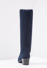 Knee-high navy blue boots made of soft suede, featuring a tapered design and a low, block heel for stability. Textured finish highlights the material.